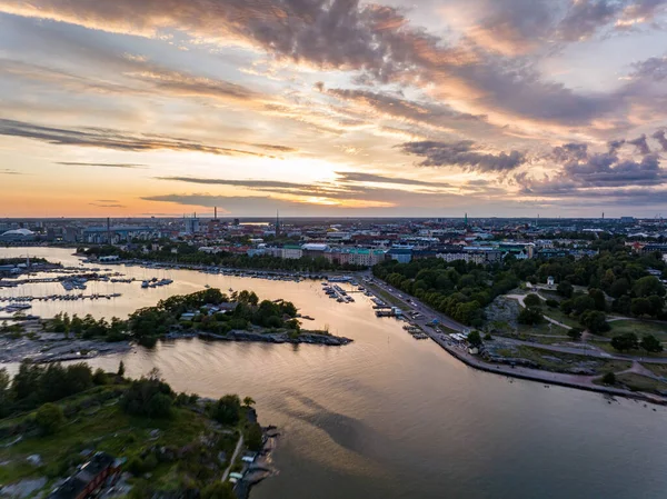 Limandaki teknelerin ve yerleşim yerlerindeki çok katlı apartmanların havadan görüntüsü. Su yüzeyindeki renkli romantik günbatımı gökyüzünün yansıması. Helsinki, Finlandiya.