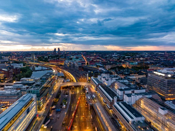 Stock image Aerial view of transport infrastructure in large city at dusk. Motion blurred shot of train station and cityscape against cloudy sunset sky. Stockholm, Sweden.