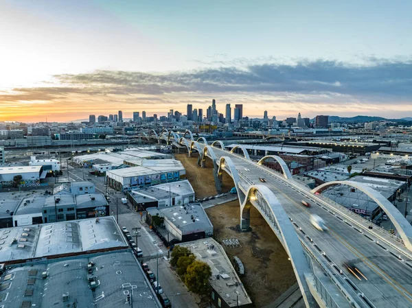 Endüstriyel kent ve modern yol köprüsünün hava panoramik manzarası. Gün batımına karşı şehir merkezindeki gökdelenlerle gökyüzü. Los Angeles, Kaliforniya, ABD.