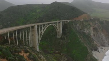 Sahildeki panoramik yoldaki yüksek köprünün hava sineması görüntüleri. Bixby Creek Köprüsü 'nden geçen arabalar. Kaliforniya, ABD.