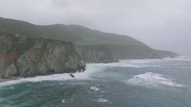 Big Sur kıyısındaki kayalık kayalıklar. Okyanus dalgaları kayalara çarpıyor. Manzarada sabah bulanıklığı. Kaliforniya, ABD.