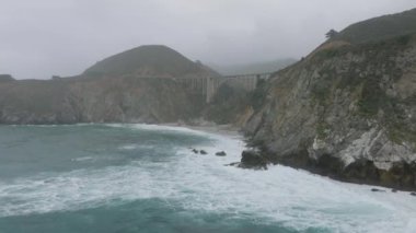 İleri sarp kayalıklar boyunca uçar. Deniz kıyısındaki vadinin üzerinde beton kemer köprüsü. Kaliforniya, ABD.