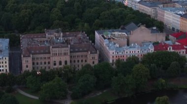 Parkta büyüyen ağaçlarla çevrili büyük sarayların havadan görünüşü. Hava kararınca şehir manzarasını ortaya çıkar. Riga, Letonya.