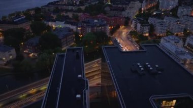 Yüksek açılı modern bina. Yukarı kaldır ve akşam şehir manzarasını ve arka plandaki su üzerindeki büyük kemer köprüsünü göster. Stockholm, İsveç.