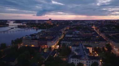 Gün batımından sonra şehir merkezindeki apartmanların havadan görünüşü. Su yolu boyunca uzanan büyük beton kemer köprüsü. Stockholm, İsveç.