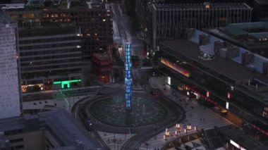 Kristall 'ın alacakaranlıktaki hava kaydırağı ve pan görüntüleri. Sergels torg meydanında fıskiyeli ikonik cam dikilitaş. Stockholm, İsveç.