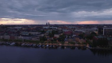 Akşam kentinde rıhtımın kaygan görüntüsü. Bankadaki teknelerin ve şehir merkezindeki binaların havadan görüntüsü. Arka planda Norra Tornen gökdelenlerinin silueti var. Stockholm, İsveç.