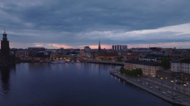 İleri, tarihi şehir merkezine yakın su yüzeyinin üzerinden uçar. Akşam kentinde kalabalık çok şeritli ana yolun havadan görüntüsü. Stockholm, İsveç.