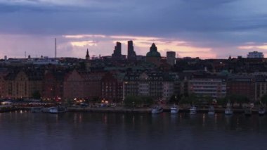 Rıhtımdaki geleneksel çok katlı apartman evleri. Norra Tornen 'in silueti günbatımına karşı modern gökdelenler. Stockholm, İsveç.