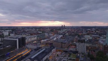 İleriye doğru alacakaranlıkta şehrin üzerinde uçar. Ana tren istasyonu çevresindeki modern binalar. Bulutlu gökyüzü ve gün batımı. Stockholm, İsveç.