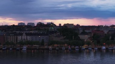 Rıhtım boyunca tekne ve binaların havadan görüntüsü. Şehrin su yüzeyi ve kenti alacakaranlıkta. Stockholm, İsveç.