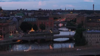 Gün batımında şehir merkezindeki tarihi binalarda su kanalı görüntüsü. Ön planda çok şeritli yolda giden arabalar. Stockholm, İsveç.