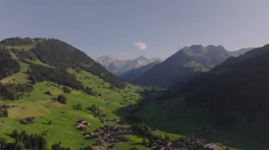 Altın saatinde güzel dağ manzarasının hava panoramik manzarası. Alp köyü ve arka planında kayalık sırt olan yeşil vadi. Gstaad, İsviçre.