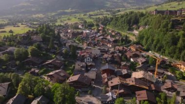 Altın saatinde küçük bir dağlık kasabadaki caddelerin ve binaların havadan görünüşü. Tepedeki tipik evler ve kiremitler. Gstaad, İsviçre.