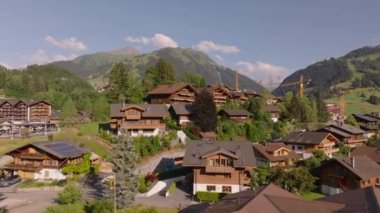 Dağ yolculuğu varış yerindeki evlerin üzerinden uç. Güneşli bir günde Alp kasabası. İnşaat alanında bir grup vinç. Gstaad, İsviçre.