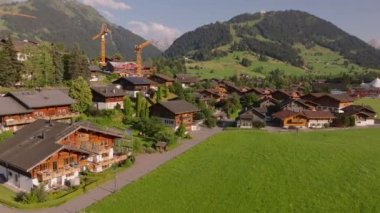 Dağ manzarasında tipik evler ve kulübelerle geleneksel dağlık şehrin hava görüntüleri. İnşaat alanında vinçler. Gstaad, İsviçre.