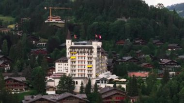 Şato tarzında lüks bir otel binasının havadan yükselen görüntüsü. Küçük dağlık kasabadaki binalar. Gstaad, İsviçre.