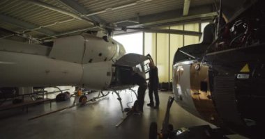 Bir çift teknisyen hangarda açık bir helikopter koruması altında çalışıyor. Uçuş öncesi bakım. Havaalanı ve havacılık kavramı.