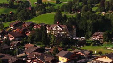 Küçük bir dağ kasabasındaki dağ otelleri ve dağ evlerinin hava kaydırak ve pan görüntüleri. Yeşil bitki örtüsüyle çevrili tipik binalar. Gstaad, İsviçre.