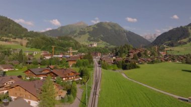 İleri, yüksek dağların arasındaki küçük dağlık alana giden yerel demiryolu hattının üzerinden uçar. Güzel manzara manzarası. Gstaad, İsviçre.