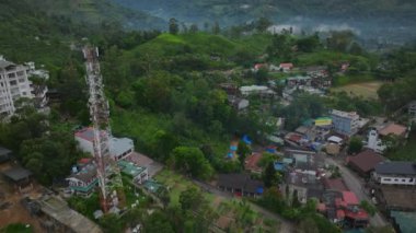 Tarlaların ve evlerin hava görüntüleri. Geriye doğru, yeşil tropikal ormanlarla çevrili tepelik arazide küçük bir şehir olduğunu gösteriyor. Ella, Sri Lanka.