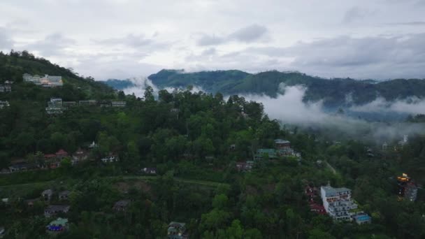 环绕着绿色植被的斜坡上建筑物的空中景致 热带旅游目的地的小镇 多云的一天 云雾从山谷中升起 Ella 斯里兰卡 — 图库视频影像