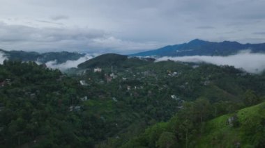 Ormanlık tepeler, orman bitkileri ve uzak bir yerde küçük bir şehir olan güzel manzaranın havadan panoramik görüntüsü. Vadiden yükselen sis ile sabah görüntüsü. Ella, Sri Lanka.