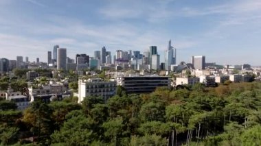 Parktaki ağaçların üzerinden uçarak lüks yerleşim yerlerini ortaya çıkarıyor. La Defense iş bölgesindeki yüksek binalar. Paris, Fransa.
