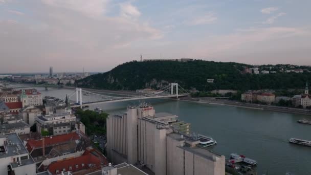 ドナウ川のウォーターフロントにあるホテルの建物の上を飛びます 美しい道路橋と歴史的なシタデラ川の上の丘 ブダペスト ハンガリー — ストック動画