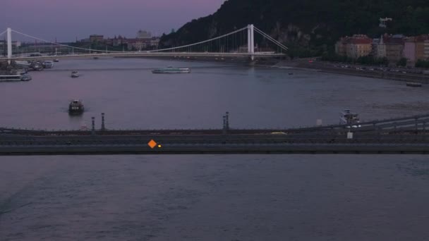 広いダヌーブ川とその橋の夕暮れの空中観察 ウォーターフロント道路を走行する車両 ブダペスト ハンガリー — ストック動画