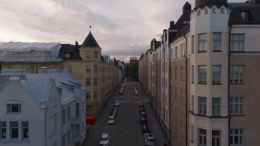 Şehir mahallesindeki caddenin üzerinde ilerliyorlar. Çok katlı apartmanların olduğu cadde boyunca park edilmiş arabalar. Helsinki, Finlandiya.
