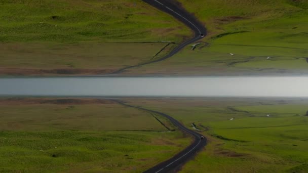 緑の牧草地を通って道路を運転する車 アイスランドのフラットな風景 抽象的なコンピュータ効果デジタル構成された映像 — ストック動画