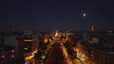 Akşamları metropoldeki geniş caddenin üzerinde ilerliyorlar. Aydınlatılmış cadde ve binaların hava görüntüleri. Paris, Fransa.