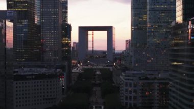 İleri, La Defense 'daki modern gökdelenler arasında uçuyor. Renkli alacakaranlık gökyüzüne karşı ünlü La Grande Kemeri. Paris, Fransa.