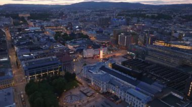Akşam kentinde binaların hava panoramik manzarası. Alacakaranlıkta Jernbanetorget Meydanı 'ndaki aydınlatılmış Ruter Yardım Merkezi. Oslo, Norveç.