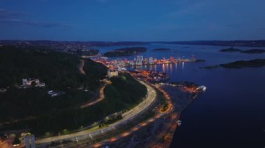 Sahil boyunca uç. Lojistik terminalle aydınlatılmış yol ve liman. Alacakaranlıkta Oslo fiyordunun havadan görünüşü. Oslo, Norveç.