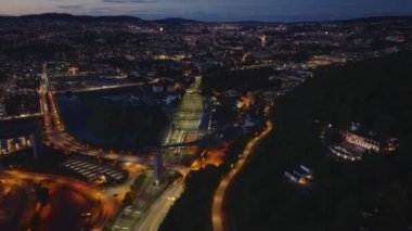 Akşam kentinde yolların ve demiryollarının hava görüntüleri. Arka planda gün batımından sonra şehir merkezindeki binalar ve tepeler gökyüzüne karşı. Oslo, Norveç.