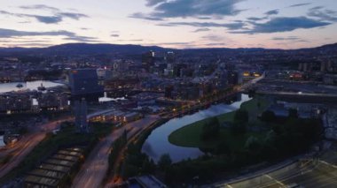 İleriye doğru alacakaranlıkta şehrin üzerinde uçun. Sokaklar ve modern şehir gelişimi ve su yüzeyi alacakaranlık gökyüzünü yansıtıyor. Oslo, Norveç.