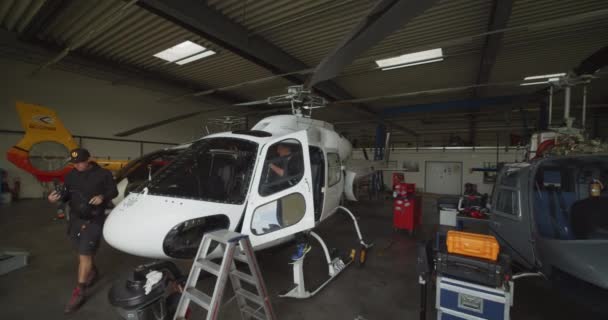 Diapositiva Panorámica Pequeño Helicóptero Blanco Estacionado Hangar Pareja Hombres Montando — Vídeos de Stock
