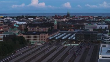 Gün batımında Central tren istasyonundaki tren ve platformların hava görüntüsü. Şehir merkezinde binalar ve arka planda turistik yerler var. Helsinki, Finlandiya.