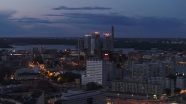 Yüksek katlı binaların ve bacalı fabrikaların hava kaydırak ve pan görüntüleri. Akşamları şehirde çeşitli binalar. Helsinki, Finlandiya.