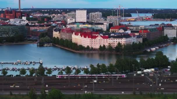 侧向跟踪现代通勤火车单位通过海湾与系泊船 背景在城市里的建筑物 芬兰赫尔辛基 — 图库视频影像