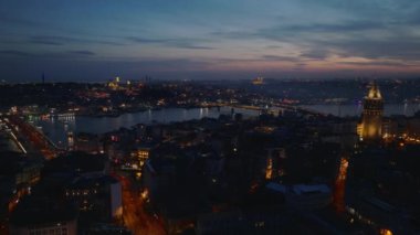 Akşam şehrinin üzerinden uç. Tarihi Galata Kulesi ve karşı kıyıdaki cami. Aydınlatılmış turistik yerler. İstanbul, Türkiye.