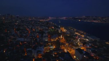 Gece şehrinin üzerinde uç. Şehir caddelerinde trafik vardı. Geniş nehir manzaralı akşam manzarası ve arka planda aydınlatılmış köprü. İstanbul, Türkiye.