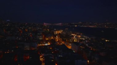 Geceleri şehir merkezindeki binaların hava kayması ortaya çıkıyor. Aydınlatılmış Boğaz Köprüsü ile akşam manzarası. İstanbul, Türkiye.