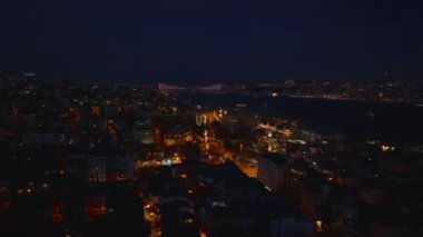 Geceleri şehir merkezindeki binaların hava kayması ortaya çıkıyor. Aydınlatılmış Boğaz Köprüsü ile akşam manzarası. İstanbul, Türkiye.