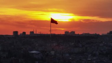 Büyük ulusal bayrağın silueti turuncu renkli günbatımı gökyüzüne karşı. Akşam karanlığında şehir manzarası. İstanbul, Türkiye.