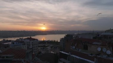 Apartman binalarının üzerinden uçuyor. Şehir ve su yüzeyinin panoramik görüntüsünü gün batımı gökyüzüne karşı gözler önüne seriyor. İstanbul, Türkiye.