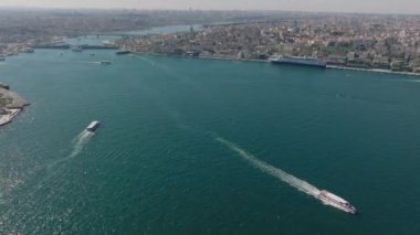 Geniş nehirde ya da boğazda hareket eden teknelerin yüksek açılı görüntüsü. Arka planda büyük bir metropol. İstanbul, Türkiye.