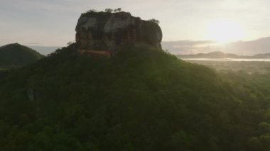 Uçsuz bucaksız tropikal ormanın üzerinde yükselen kayaların görüntülerini geri çek. Popüler Lions Rock, yükselen güneşe karşı. Sigirya, Sri Lanka.